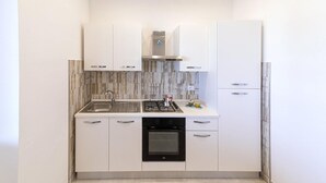 Eine moderne Küche mit weißen Schränken, einer Edelstahl-Spüle, einem Gasherd und einem eingebauten Backofen.