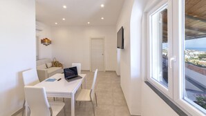 Ein modernes Zimmer mit Esstisch, Stühlen, einem Laptop und einem Fernseher an der Wand.