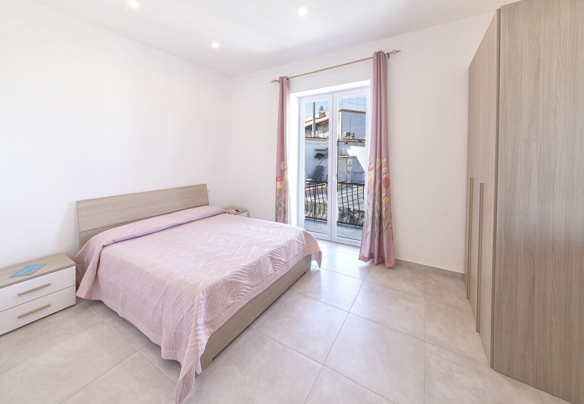 A bedroom with a bed, a nightstand, a wardrobe, and a sliding glass door to the outside.
