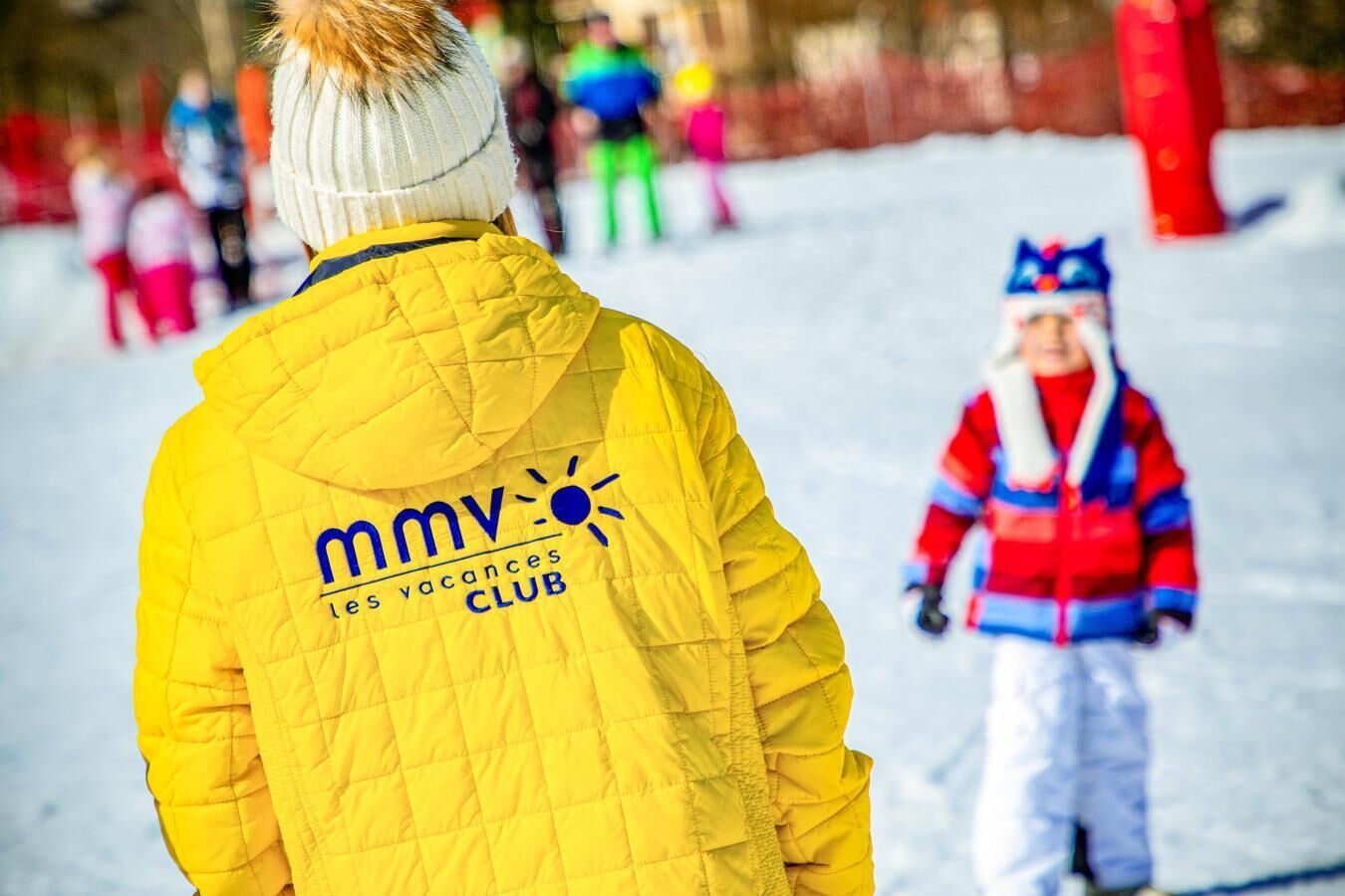 Eine Person in einer gelben Jacke mit einem Aufdruck auf dem Rücken steht in verschneiter Landschaft.