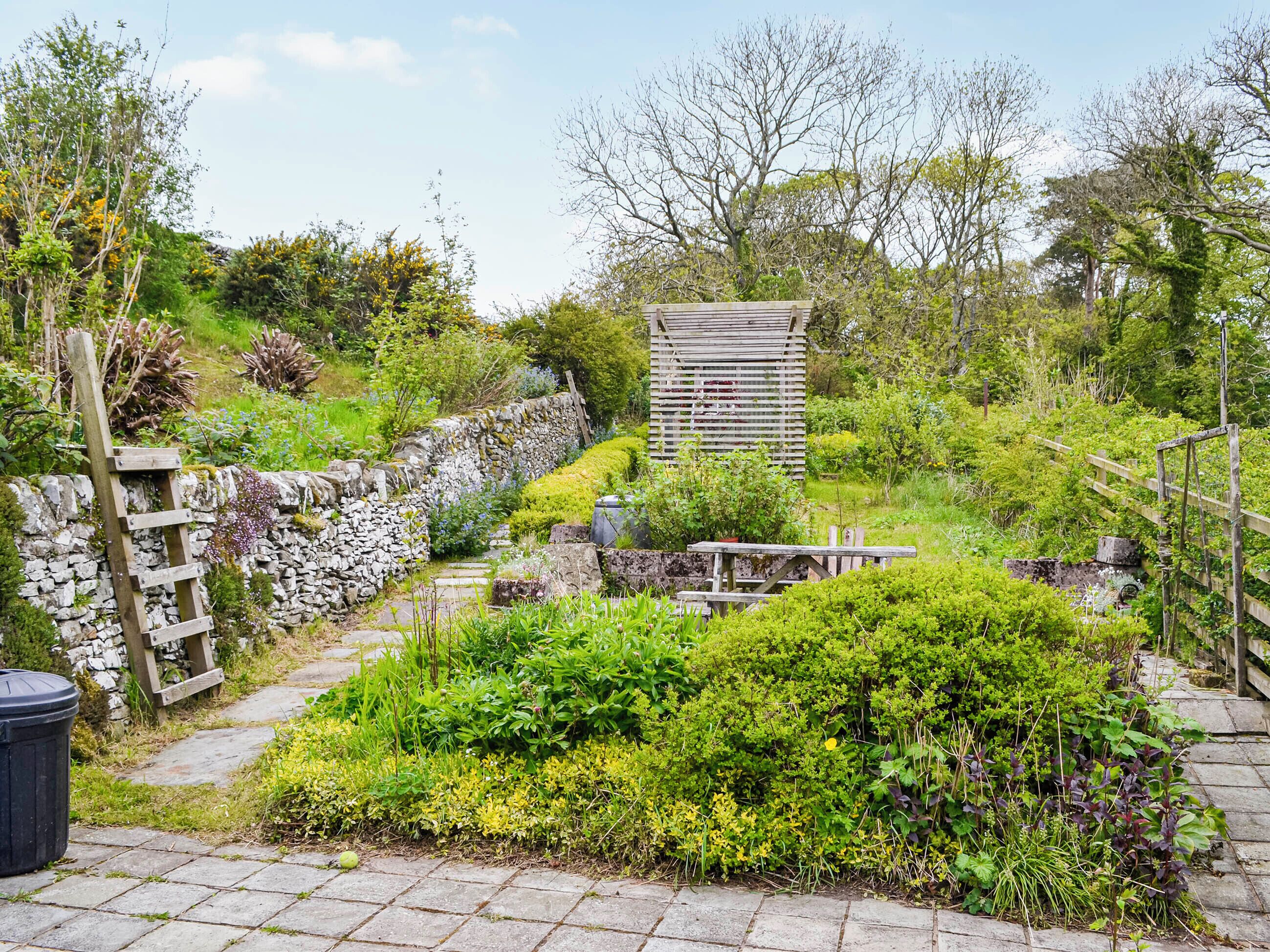 A garden with stone walls, a wooden bench, and a wooden structure.