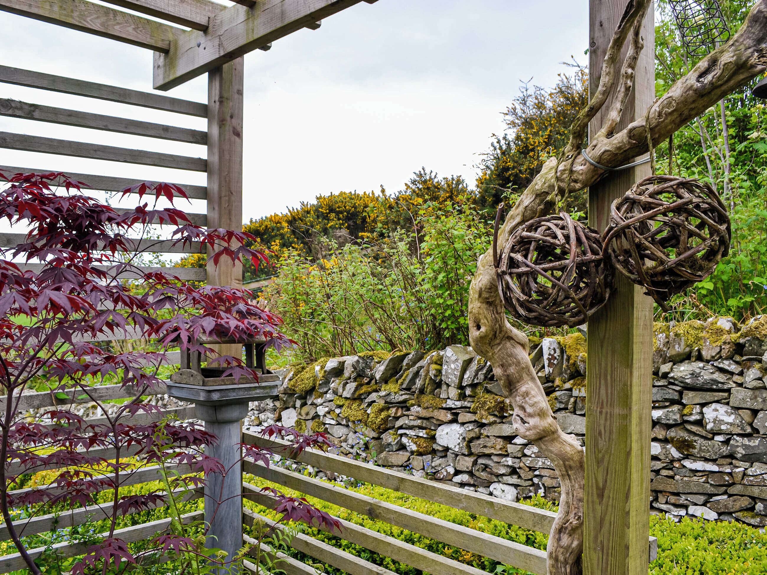 A wooden pergola with a stone wall and a stone pathway.