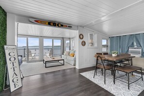 A spacious living area with a large window, a wooden dining table, and a couch. - Lakeside Cottage ~ Pool, Hot tub & Private Beach (Colchester)