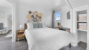 A bedroom with a large bed, a bedside table with a lamp, a chair, and a wall decorated with circular patterns. - Lakeside Cottage ~ Pool, Hot tub & Private Beach (Colchester)