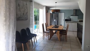 A dining area with a table and chairs, a kitchen in the background, and a sliding glass door leading to a balcony. - Villa with private pool (secure) pétanque court-Mont Ventoux - Last minute (Modène)