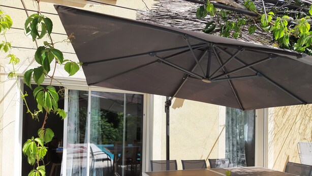 An outdoor patio with a table and chairs, a large umbrella, and a sliding glass door leading to an interior space. - Villa with private pool (secure) pétanque court-Mont Ventoux - Last minute (Modène)