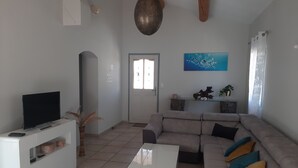 A living room with a sofa, a coffee table, a TV on a stand, a decorative plant, and a painting on the wall. - Villa with private pool (secure) pétanque court-Mont Ventoux - Last minute (Modène)