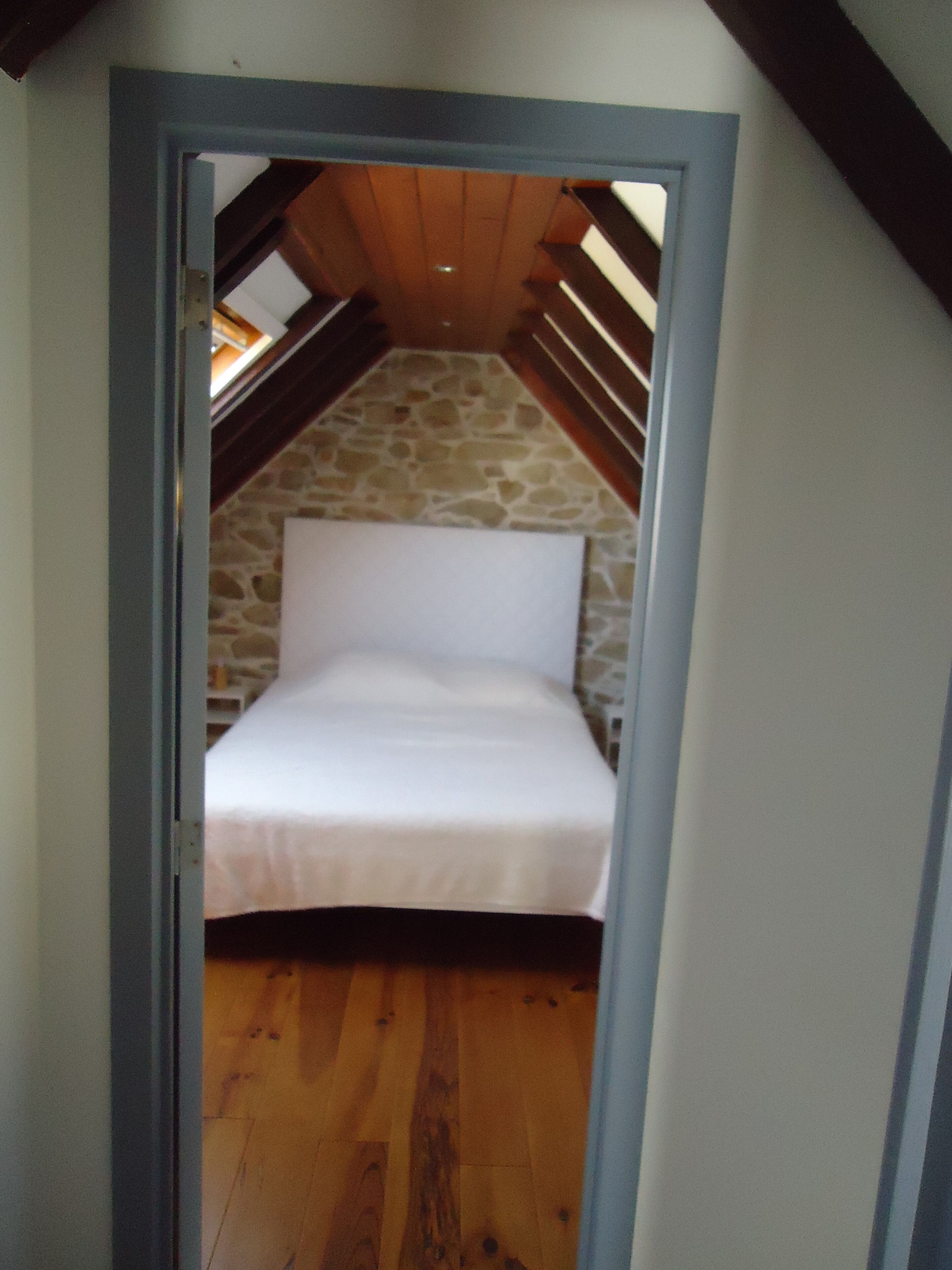 A bedroom with a stone wall, wooden floor, and a sloped ceiling.