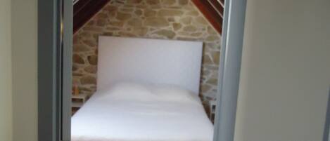 A bedroom with a stone wall, wooden floor, and a sloped ceiling.