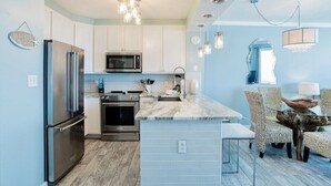A modern kitchen with stainless steel appliances, a marble island, and wicker chairs. - Silver Beach 504 | Updated, Direct Beach Front, Pet Friendly! (Orange Beach)