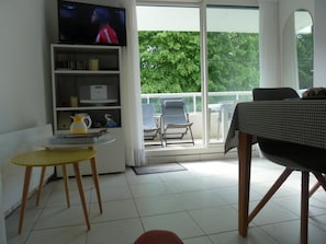 A modern living room with a television, a bookshelf, a small table, and a balcony with a chair.