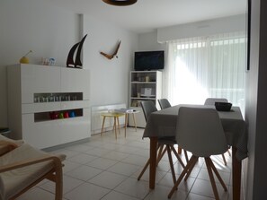 A modern, well-lit room with a dining table, chairs, a bookshelf, and a TV.