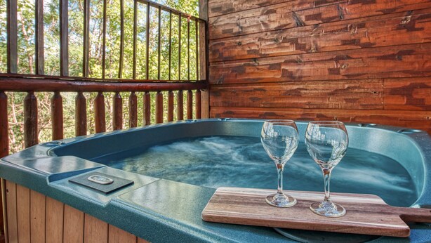 Un jacuzzi con dos copas de vino vacías sobre una bandeja de madera, rodeado de paredes y barandilla de madera.