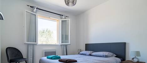 A modern bedroom with a large bed, a chair, a nightstand, and a window with curtains.