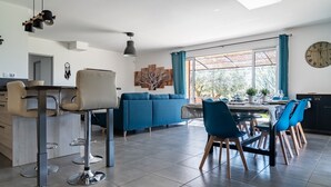 A modern kitchen with a dining area, featuring a blue sofa, a dining table with chairs, and a large window with curtains.