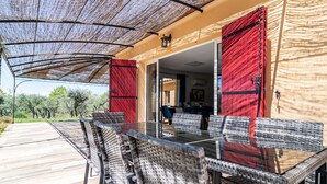 An outdoor dining area with wicker chairs and a glass table, covered by a woven shade.