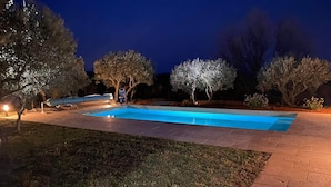 A rectangular swimming pool with a paved deck, surrounded by well-maintained grass and trees.