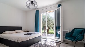 A bedroom with a bed, a chair, a patterned rug, and a view through a glass door.