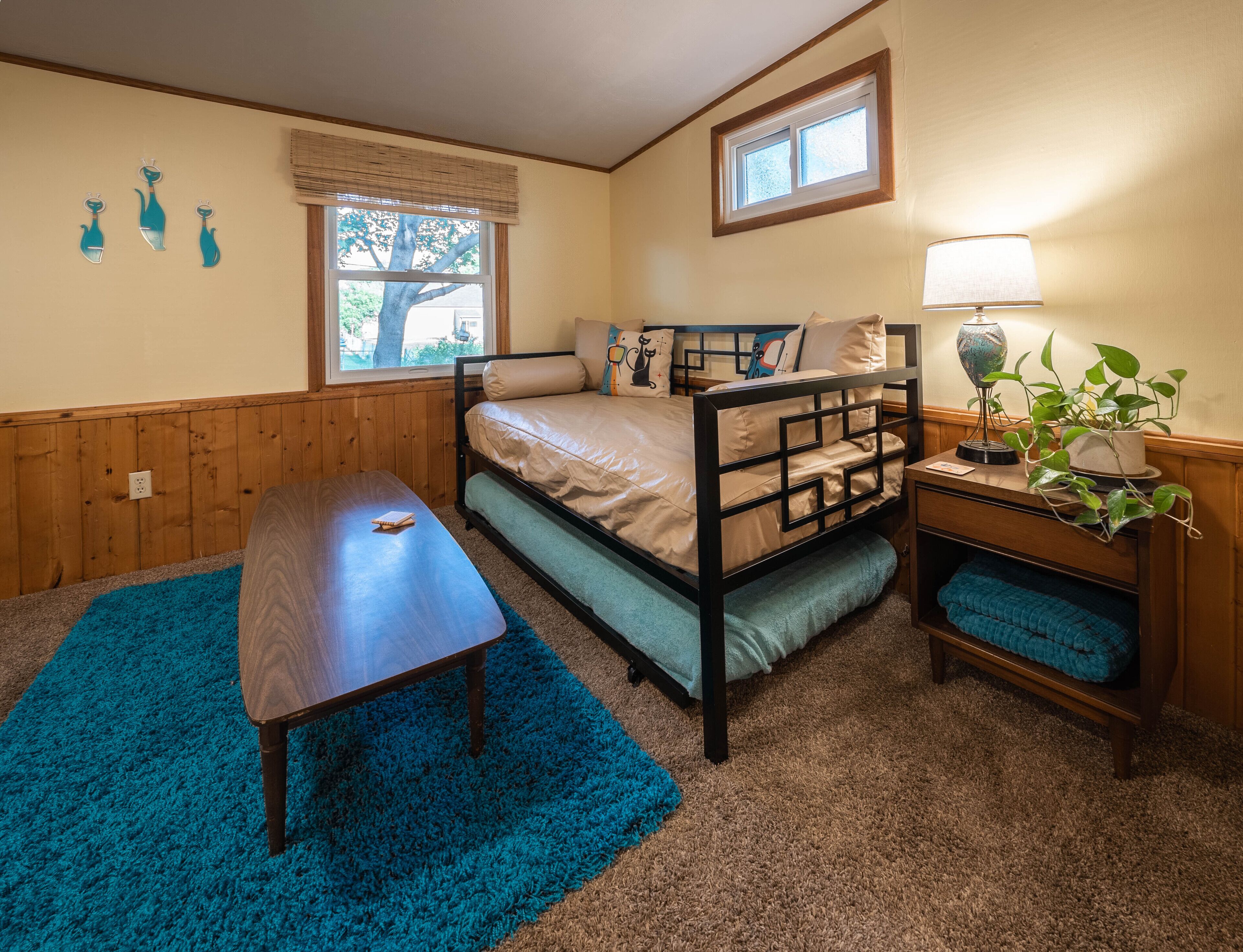 Un dormitorio con una litera, una mesita de noche con lámpara, una ventana con persianas y una alfombra azul.