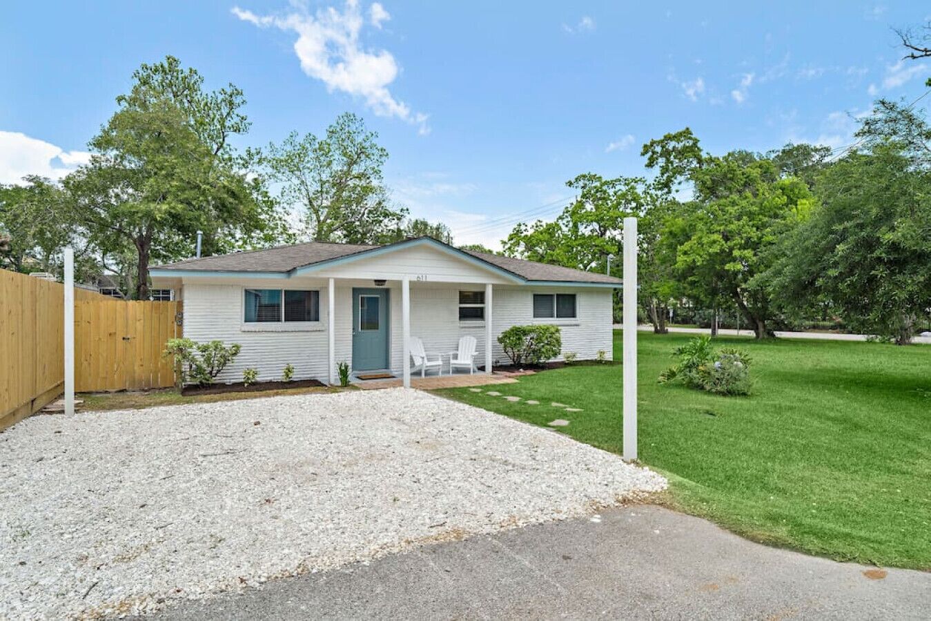 A single-story mobile home with a front porch, a small lawn, and a wooden fence.