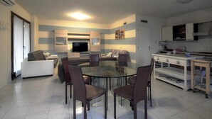 Una cocina moderna con comedor, que incluye una mesa de vidrio y sillas marrones, un horno empotrado y un televisor montado en la pared.