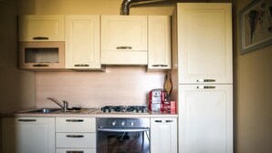 Eine kleine Küche mit weißen Schränken, einem Gasherd, einem Backofen und einer Kaffeemaschine.