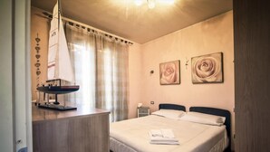 Ein Schlafzimmer mit einem Bett, einem Nachttisch mit Lampe, zwei weiteren Nachttischen und zwei Wandbildern mit Rosenmotiven.