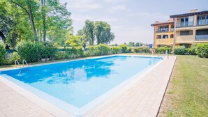A rectangular swimming pool with a tiled deck, surrounded by greenery and a multi-story building with balconies. - La Moderna Egman - Italian Homing (Sirmione)