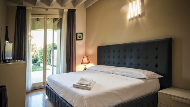 A bedroom with a large bed, a bedside table, a lamp, and a TV on a cabinet. - La Moderna Egman - Italian Homing (Sirmione)