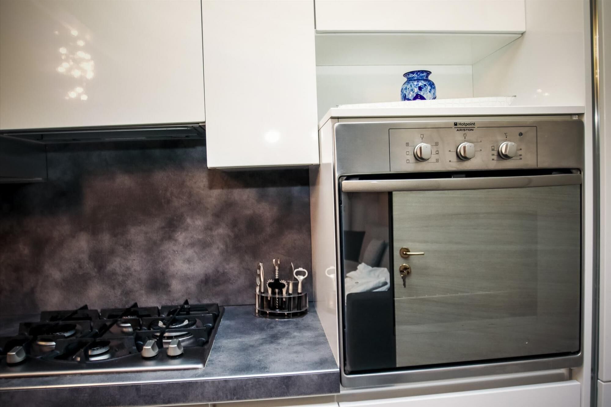 Uma cozinha com fogão a gás, forno e um vaso azul na bancada.