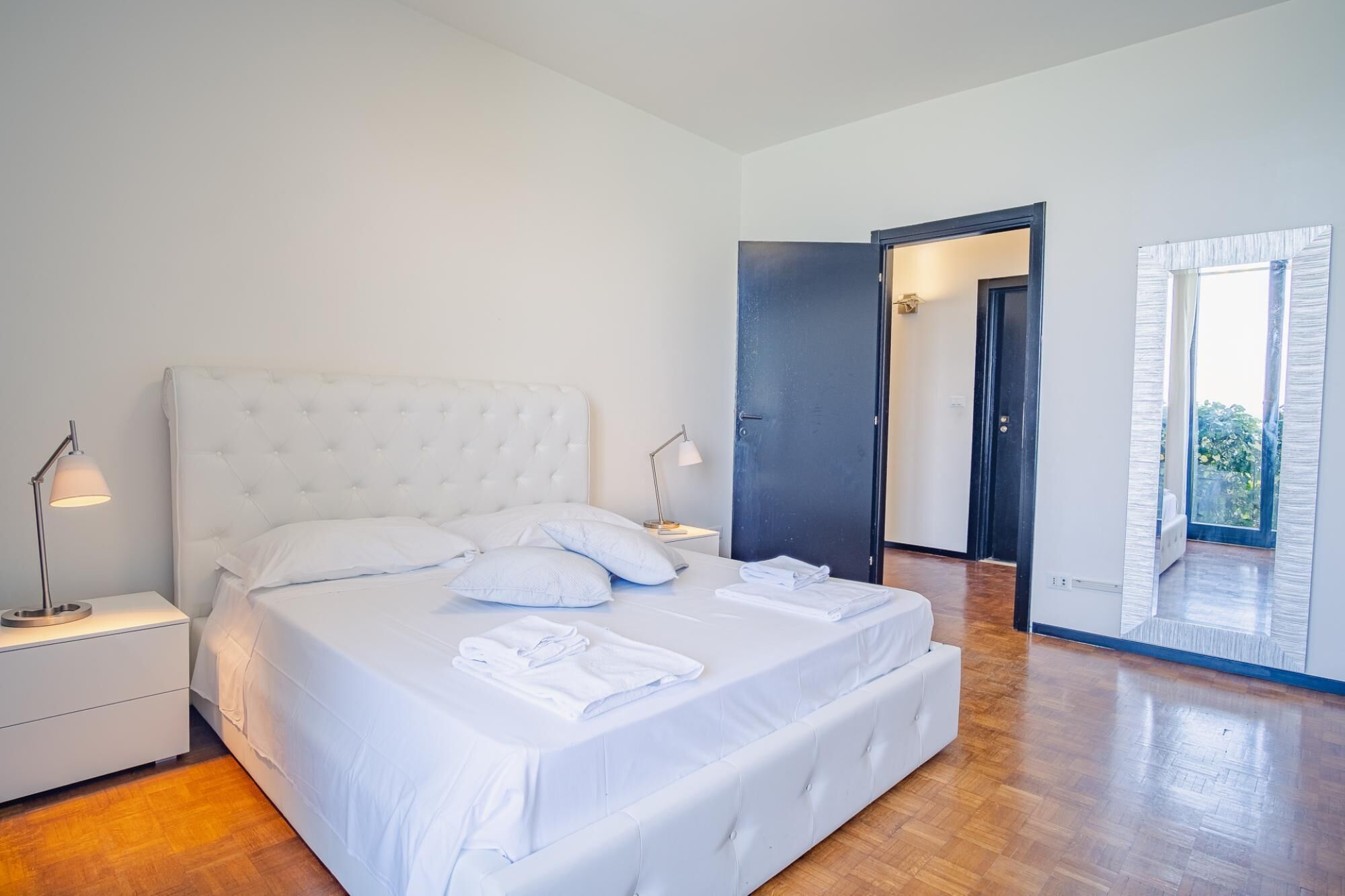 Et soveværelse med en stor seng, to sengeborde og en dør til en balkon.