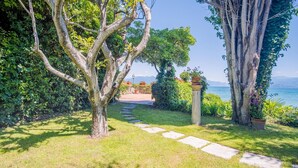 A garden pathway leading to a scenic view of a lake with mountains in the background. - Villa Patrizia Lake View - Italian Homing (Desenzano del Garda)