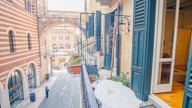 A narrow alleyway with a brick building on the left, a covered outdoor seating area in the center, and a building with blue shutters on the right. - Residenza Dei Signori - Italian Homing (Verona)