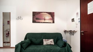Un sofá verde con cojines estampados en una habitación con un cuadro en la pared que muestra un atardecer sobre el agua.