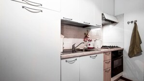 Una cocina compacta con armarios blancos, un lavamanos de acero inoxidable, una estufa a gas y un microondas.