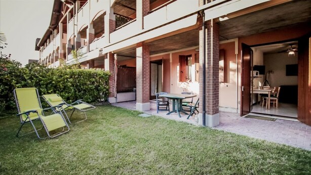 Un edificio con un espacio exterior cubierto que incluye una mesa y sillas, un pequeño jardín y vistas a una habitación con una mesa de comedor y sillas.