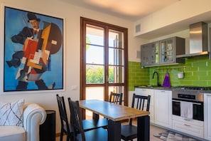Une cuisine moderne avec un coin repas, un dosseret de carrelage vert et un grand tableau abstrait.