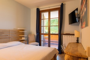 A bedroom with a bed, a chair, a table, a TV, and a view of the outdoors.