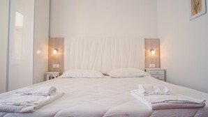 A neatly made bed with white linens and towels, two bedside tables with lamps, and a window with sheer curtains. - The Secret Garden - Italian Homing (Padenghe sul Garda)