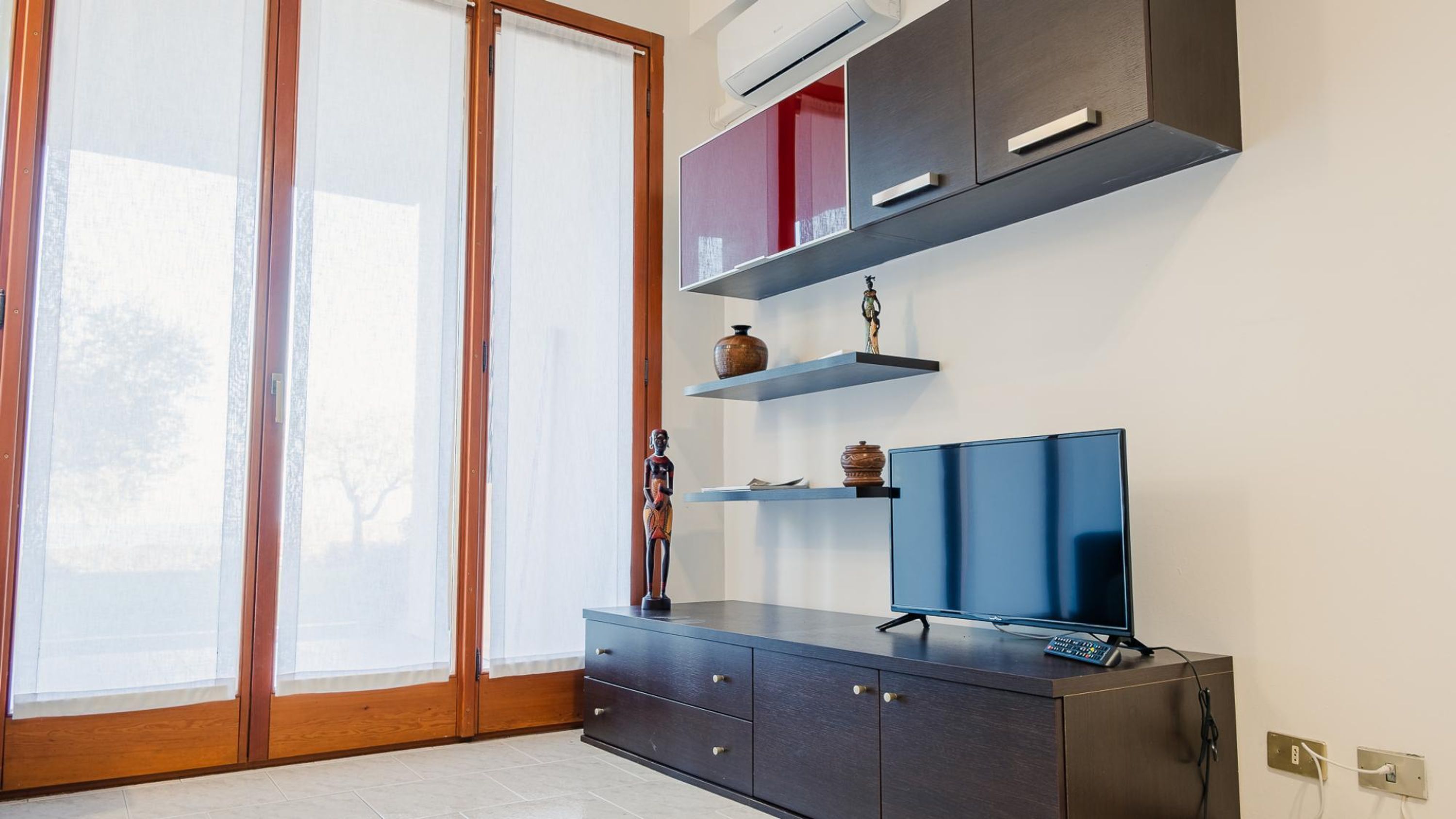 Ein modernes Wohnzimmer mit großem Fernseher, Holzschrank und Regalen mit Dekoration.