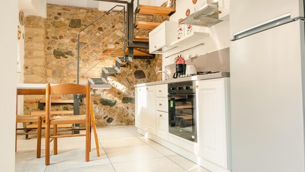 A kitchen with white cabinets, a built-in oven, and a stone wall. - La Casa di Nonna Agnese - Italian Homing (Padenghe sul Garda)