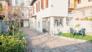 A courtyard with a stone pathway, a small garden with yellow flowers, and a table with chairs. - La Casa di Nonna Agnese - Italian Homing (Padenghe sul Garda)