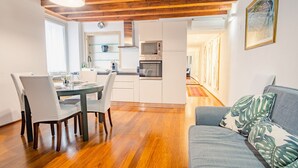 Una cucina moderna con mobili bianchi, forno integrato e microonde. C'è una zona pranzo con tavolo e sedie, e un soggiorno con divano e una pianta.