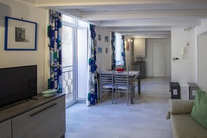 A modern living room with a television, a dining area with chairs and a table, and a kitchen area with cabinets and a phone. - Sr-i754-cman47a1 - Maniace Homes - Federico Apartment (Syracuse)