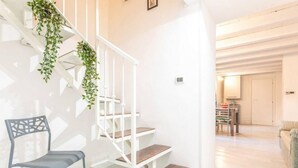 Un escalier avec des rampes blanches et des marches en bois, une chaise grise et un coin repas avec une table et des chaises.