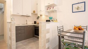 A compact kitchen with white cabinets, a small island, and a dining area with a metal chair and table.