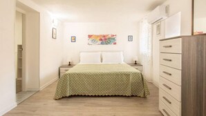 A bedroom with a bed, a dresser, a nightstand, and a wall with a painting.