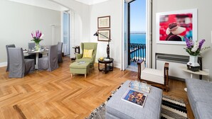 A modern living room with a dining area, a green armchair, a small table with a lamp, and a view of the sea through an open door. - Aretusa Exclusive Sea View (Syracuse)