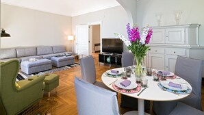 A modern living room with a grey sofa, a dining table set for four, and a kitchen area with white cabinets. - Aretusa Exclusive Sea View (Syracuse)