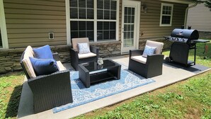 A patio with wicker furniture, a grill, and a stone wall.